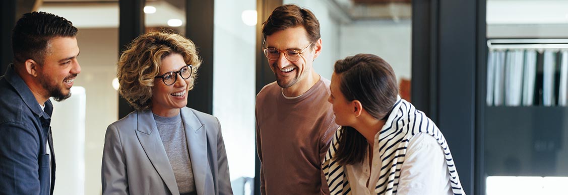 A diverse group of individuals collaborates around a laptop, engaged in discussion and sharing ideas.