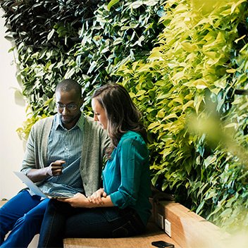 Businessman and woman sitting in front of green plant wall, using laptop