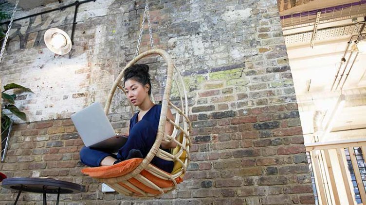 Women sitting on hanging chair and working on a laptop in office area