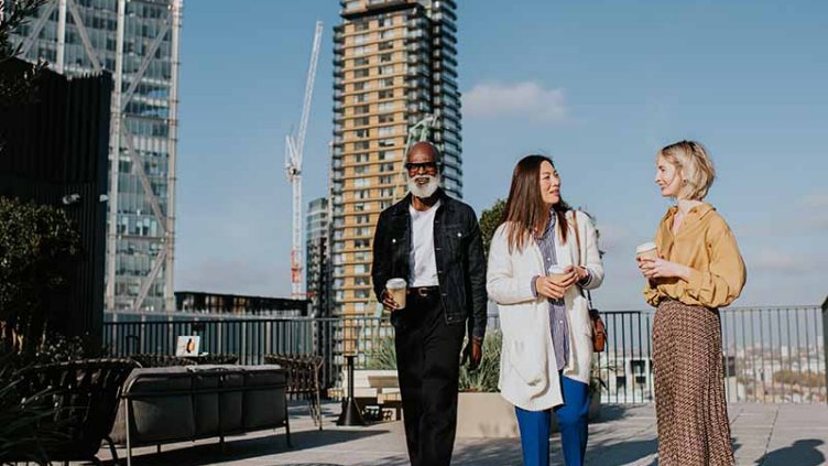 Three people in smart-casual business attire walk together on a roof top