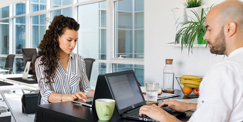 A man and a woman sitting on opposite sides of the desk, working on computers.